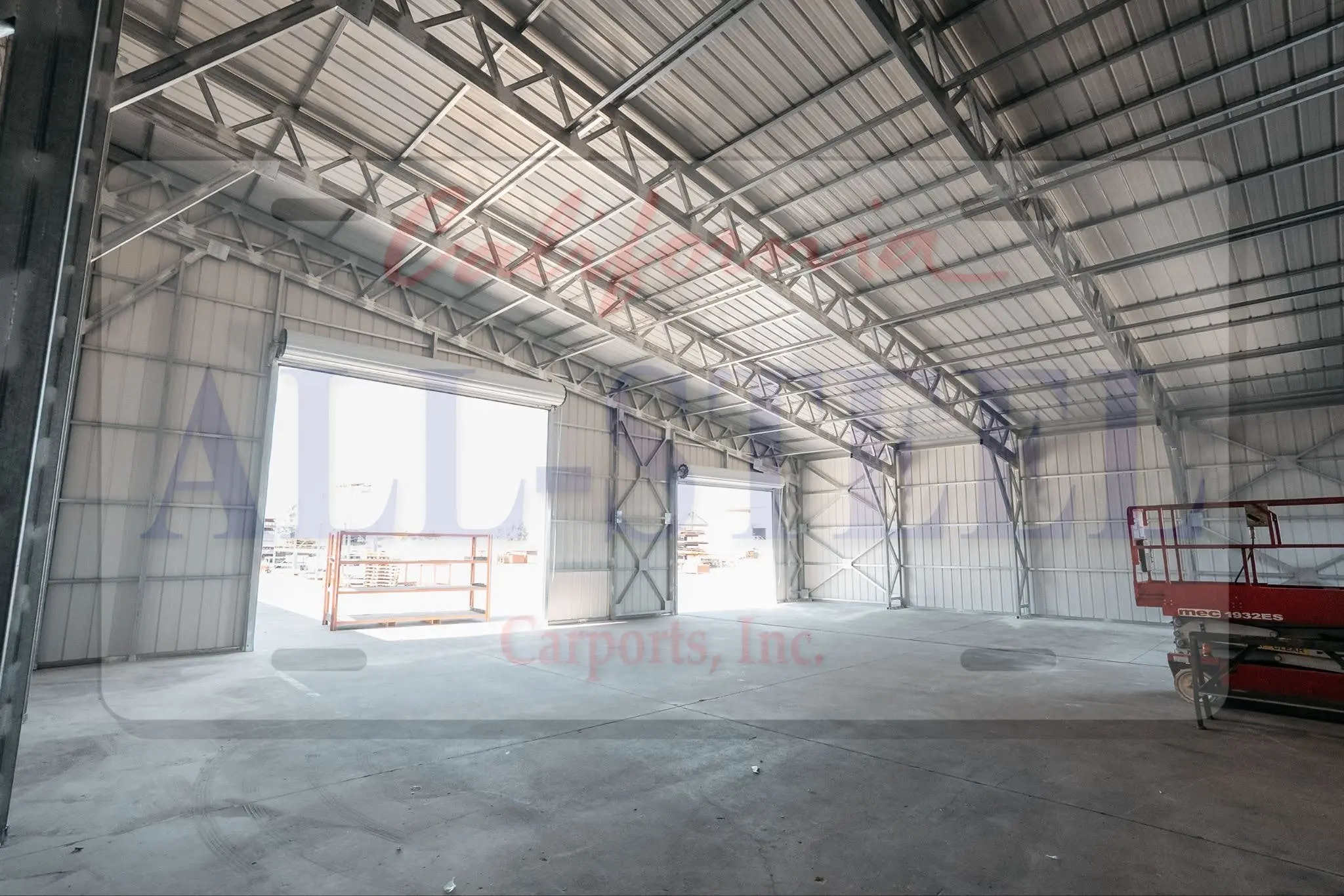 Interior angle, two roll-up doors open, a scissor lift and metal shelving unit visible near the entrance.