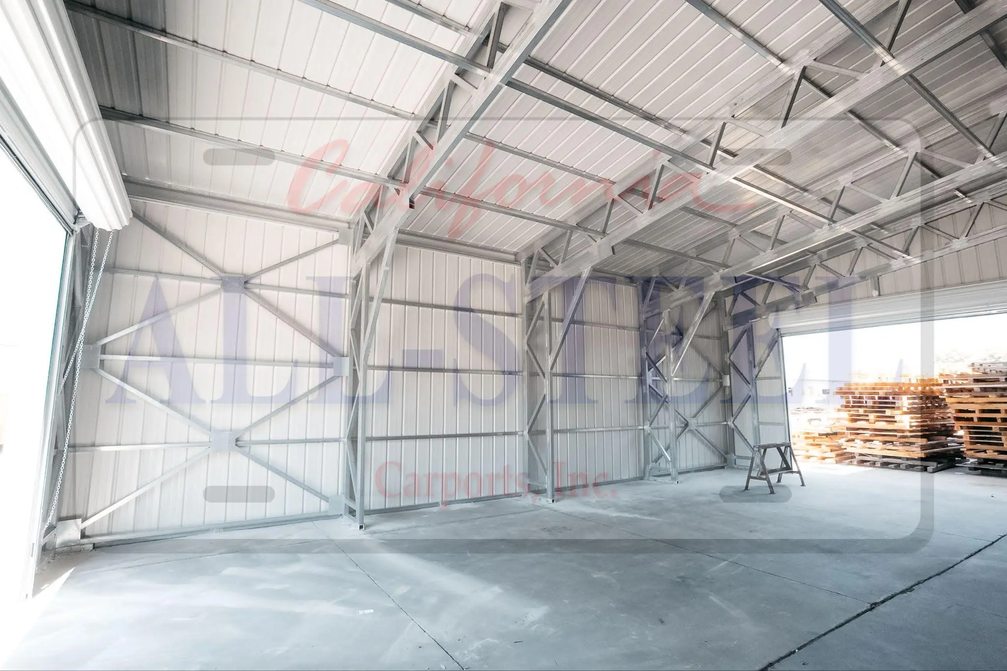 Interior shot with visible cross-braced support columns spaced along the length, roll-up door open to a yard with stacked pallets.