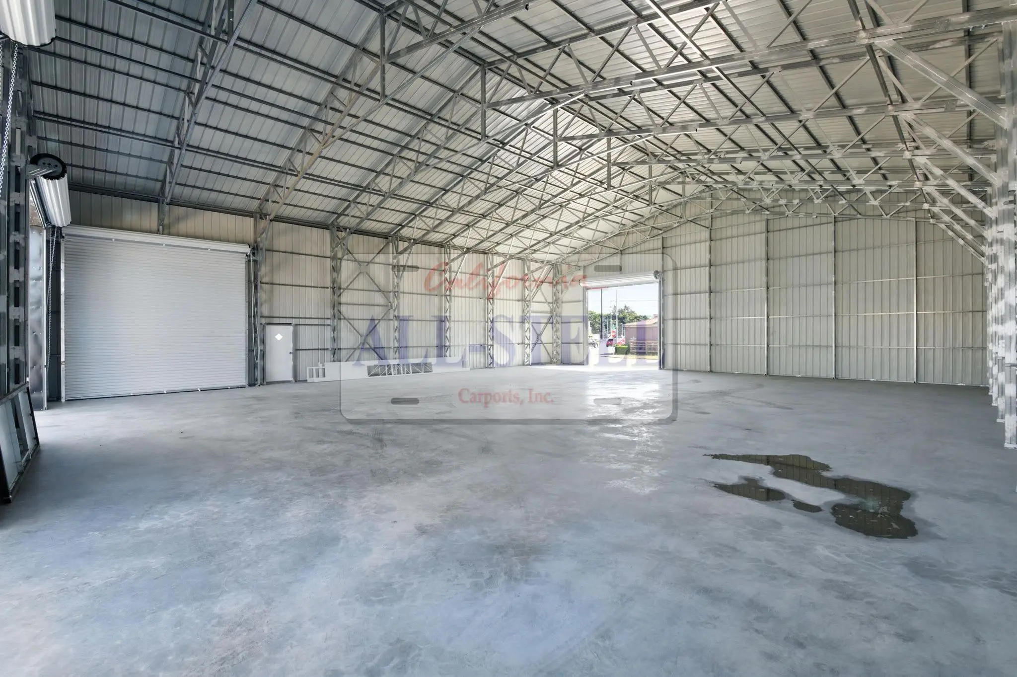 Interior shot, open truss roofline spanning the full width with no center support columns, one open roll-up door, empty concrete floor.